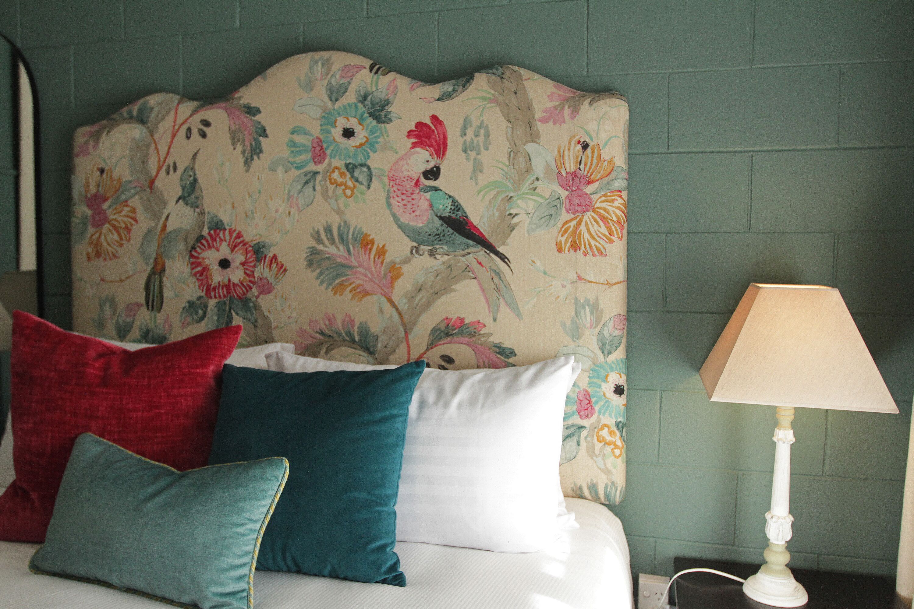 Un lit avec une tête de lit à motifs floraux, plusieurs oreillers et une table de chevet avec une lampe.