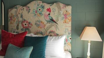 Un lit avec une tête de lit à motifs floraux, plusieurs oreillers et une table de chevet avec une lampe.