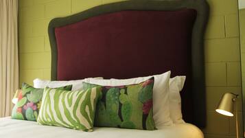 A bed with a dark headboard, white pillows, and a green pillow with a cactus pattern.