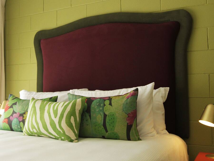 A bed with a dark headboard, white pillows, and a green pillow with a cactus pattern.