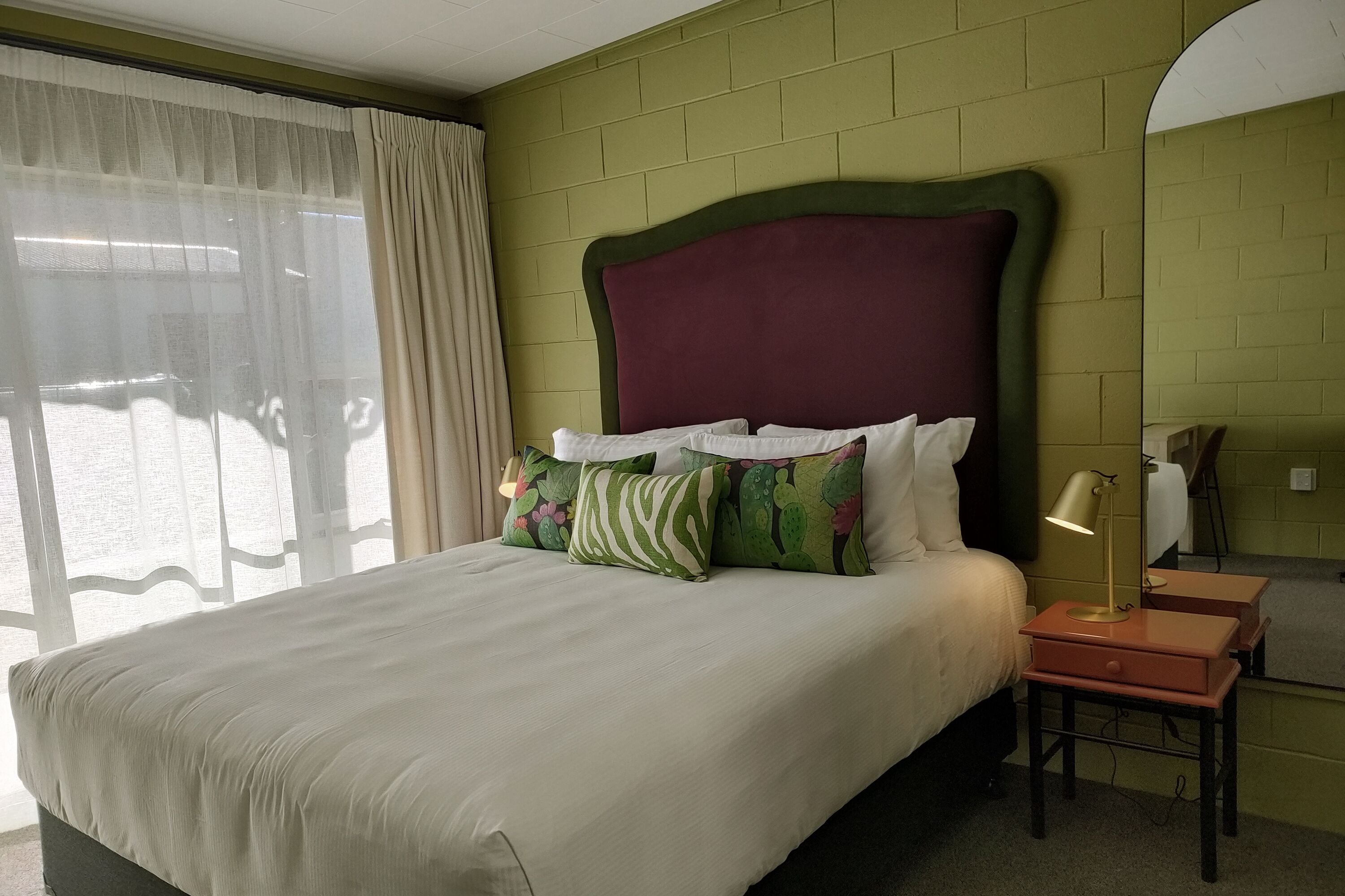 A neatly made bed with a green and white patterned pillow, a bedside lamp, and a small table.