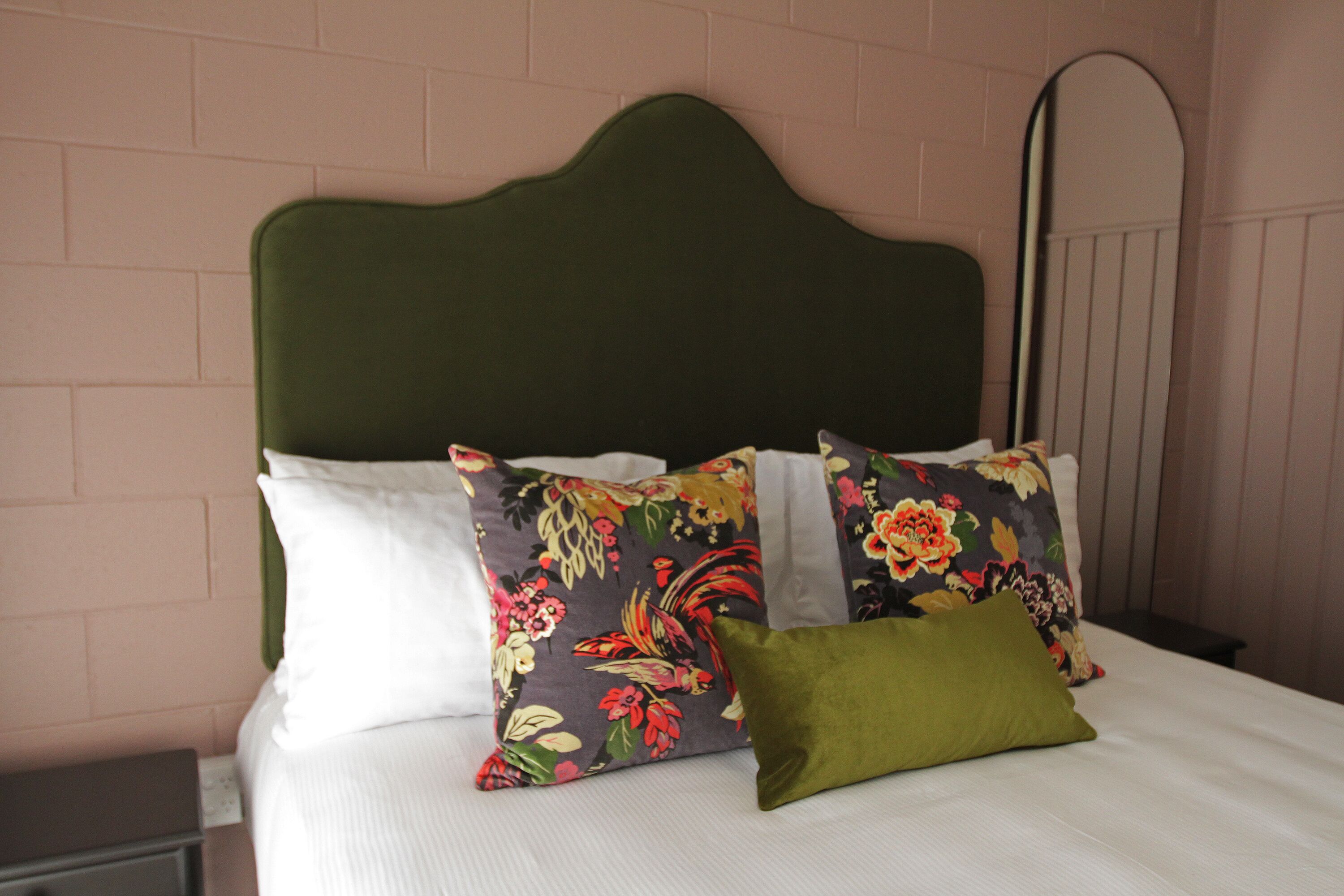 A bed with floral pillows and a green headboard in a room with pink brick walls.