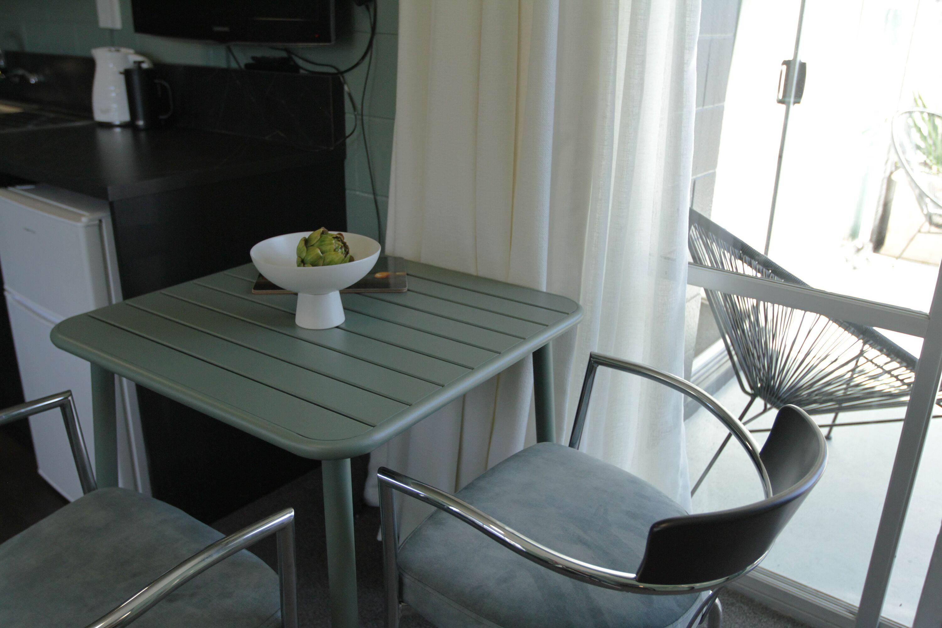 A small kitchenette with a coffee maker, a bowl of fruit, and a dining area with a table and two chairs.