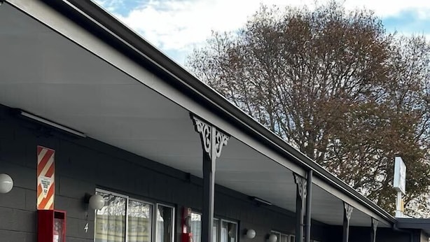 Un bâtiment doté d’un espace extérieur abrité avec des tables et des chaises en bois, ainsi que d’un extincteur fixé au mur.