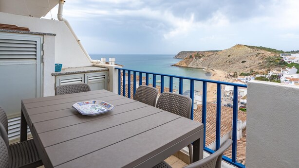 Ein Balkon mit Tisch und Stühlen mit Blick auf einen Strand und eine Küstenstadt.