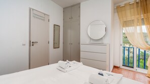 Ein Hotelzimmer mit Bett, Schrank, Spiegel und Fenster mit Blick auf Grünflächen.