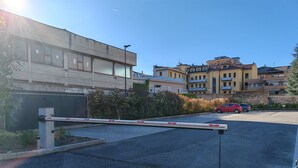 Een omheind parkeergebied met een slagboom, een rode auto en gebouwen op de achtergrond.