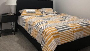 Un dormitorio con cama, mesita de noche, lámpara y ventana.