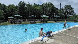 A swimming pool with people, including a child and an adult, in the water. There are picnic tables and umbrellas in the background. - Your Best Vacation is waiting at the Sage Chalet - Close to Kalahari & Camelback (Long Pond)
