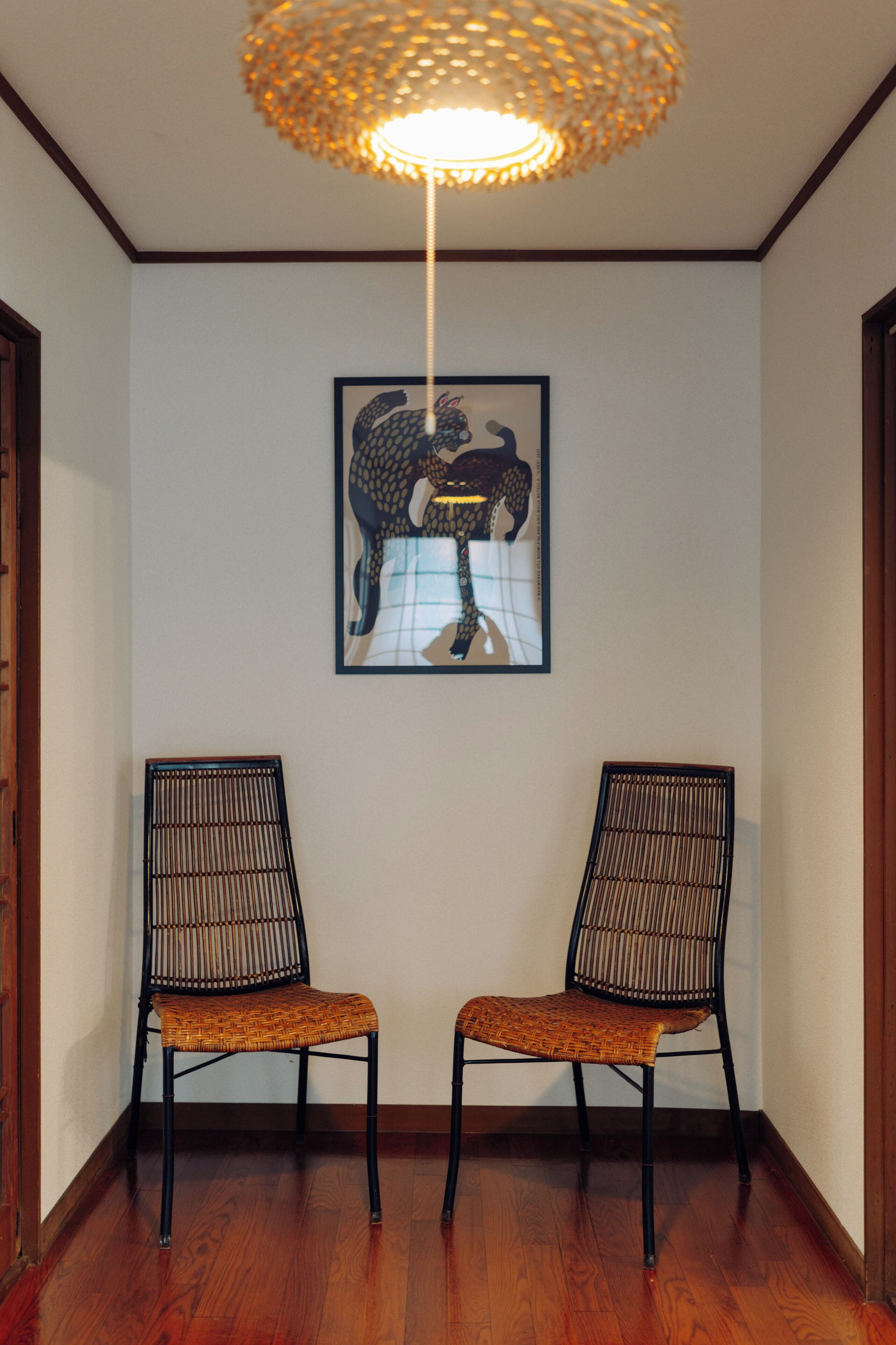 A hallway with two chairs, a framed artwork on the wall, and a hanging light fixture.