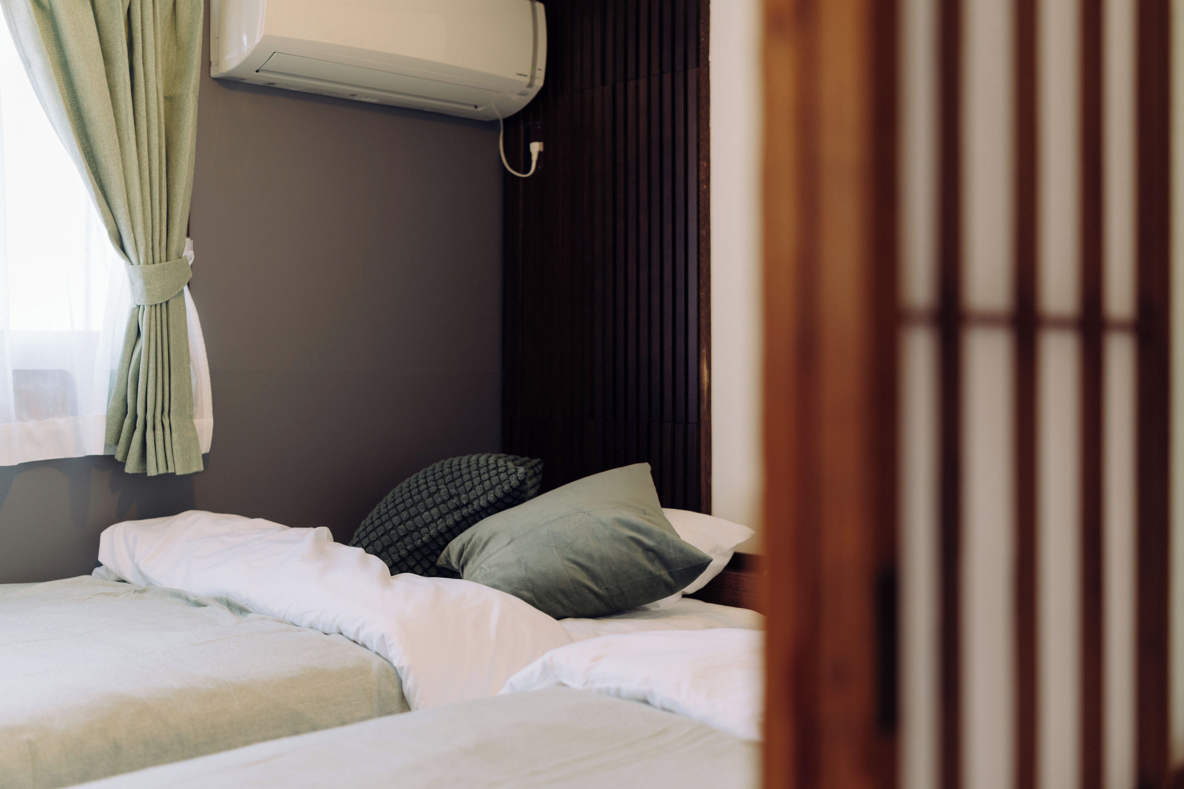 Habitación de hotel con cama, almohadas, unidad de aire acondicionado y ventana con cortinas.
