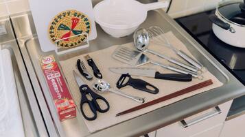 A kitchen counter with various utensils, a white bowl, a pot on the stove, and a box of food items.
