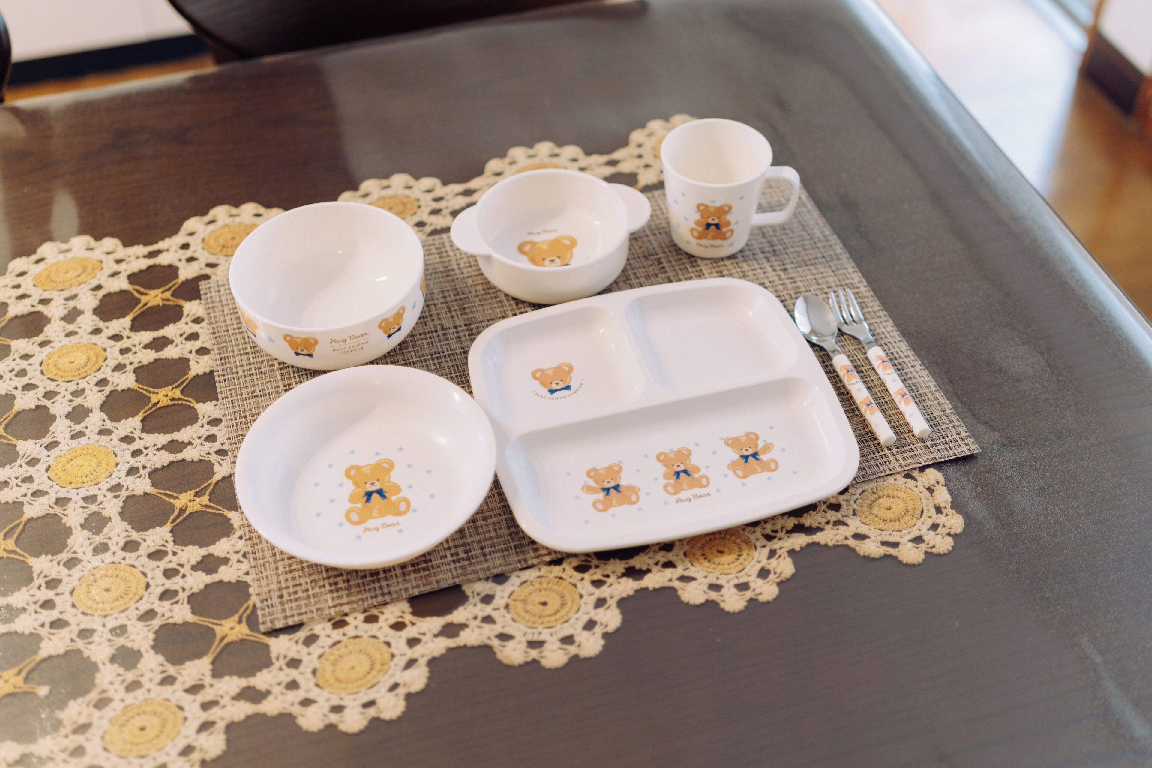 A table set with white dishes featuring bear designs, a doily, and a placemat.