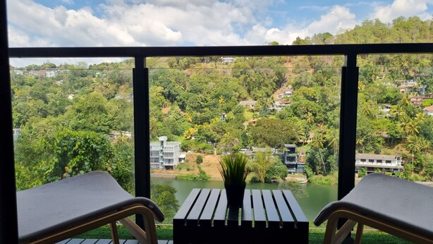 Un balcón con dos sillas y una mesa, con vistas a un paisaje verde exuberante con casas y una masa de agua.