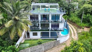 Un edificio de varios pisos con piscina, rodeado de abundante vegetación.
