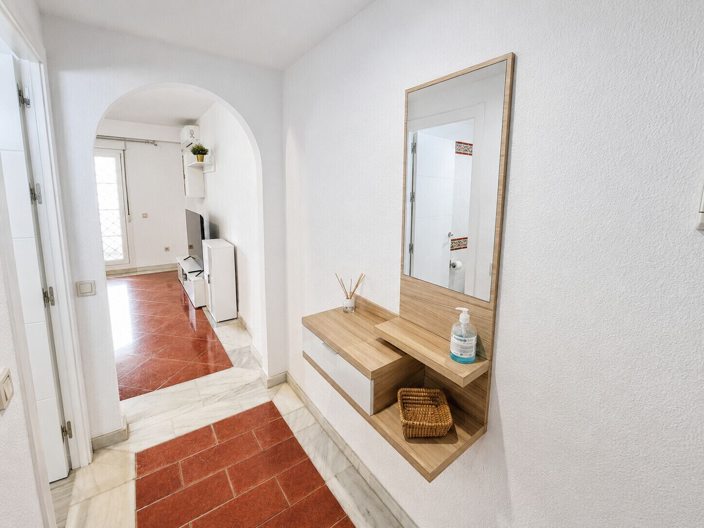 A hallway with a wooden bench, a mirror, and a small shelf with a bottle.
