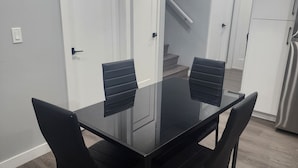 A modern dining area with a glass-top table and black chairs, a white door, and a kitchen with a stainless steel refrigerator. - Home in Northwest Calgary. (Calgary)