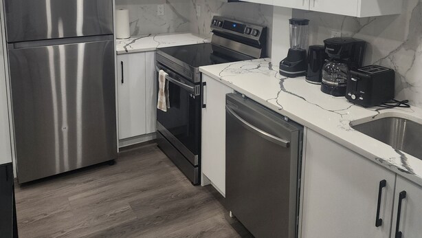 A modern kitchen with stainless steel appliances, white cabinets, and a marble countertop. - Home in Northwest Calgary. (Calgary)