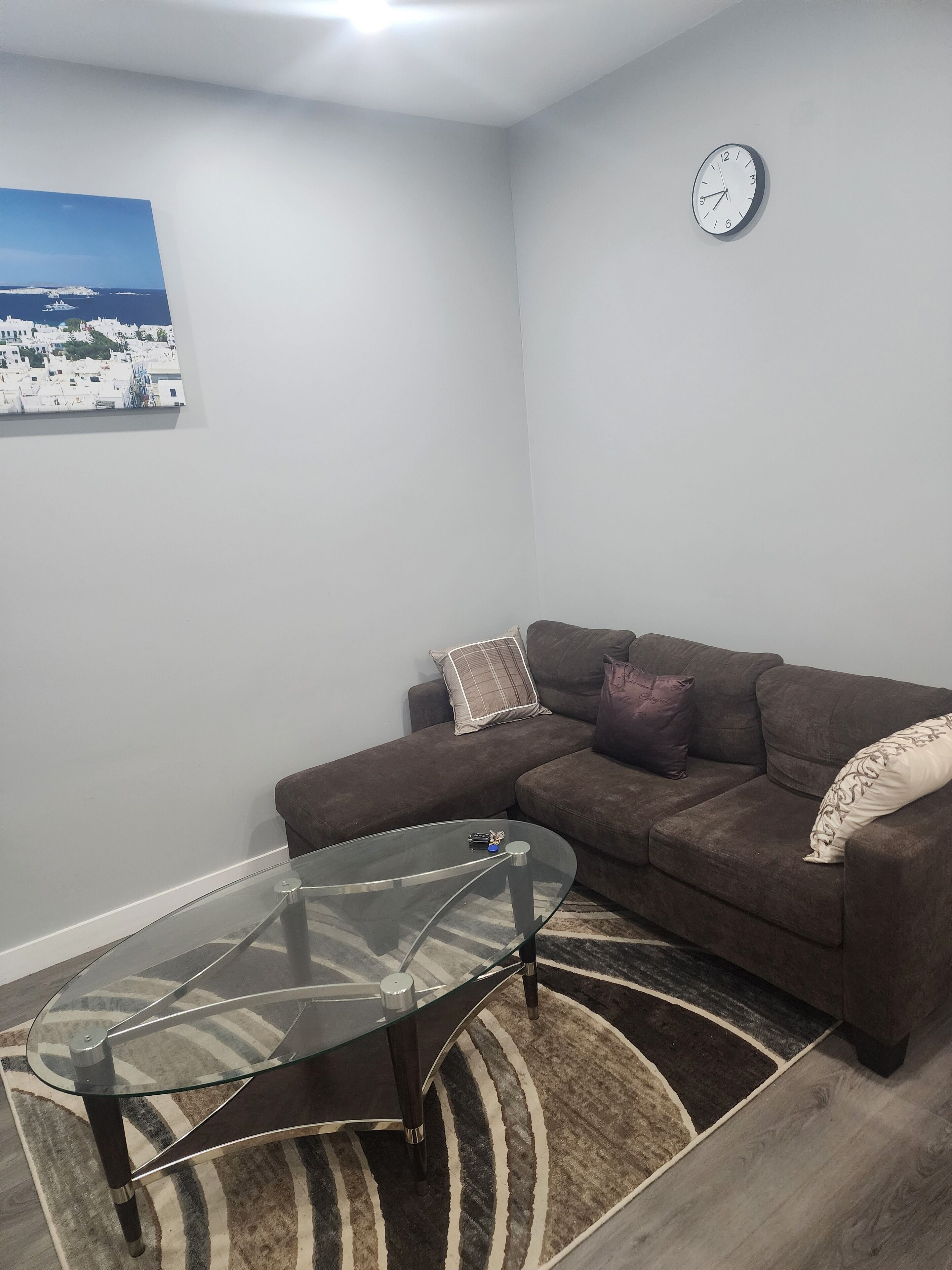 Ein Wohnzimmer mit einem Glastisch, einem braunen Sofa, einem Teppich und einer Uhr an der Wand.