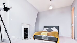 A bedroom with a bed, a fireplace, a tripod, and a hanging light fixture.