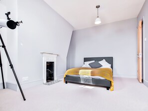 A bedroom with a bed, a fireplace, a tripod, and a hanging light fixture.