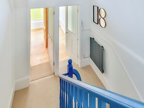 A staircase with a blue handrail leading to a landing where a radiator is mounted on the wall.