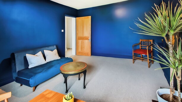 A room with a blue wall, a wooden table, a sofa, a chair, and a potted plant.