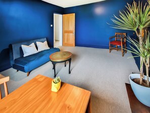 Una habitación con pared azul, una mesa de madera, un sofá, una silla y una planta en maceta.