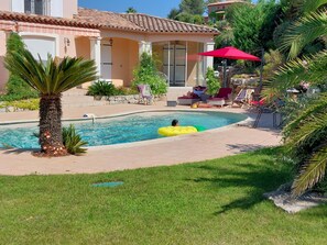 Une piscine avec un palmier, une personne sur un flotteur jaune et un parasol rouge.