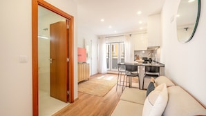 A modern apartment with a wooden door, a kitchen with a dining area, and a living room with a sofa and a mirror. - GuestReady – Timeless Lisbon Retreat (Lisbon)