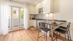 A modern kitchen with a central island, two bar stools, and a view through a glass door to an outdoor balcony. - GuestReady – Timeless Lisbon Retreat (Lisbon)