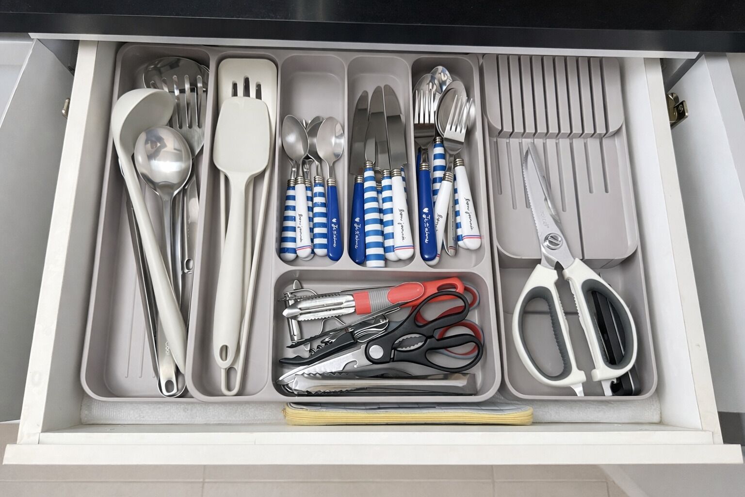 A drawer containing various kitchen utensils including spoons, forks, knives, and scissors.