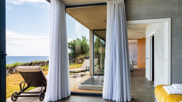 A modern bedroom with a large sliding glass door leading to a balcony overlooking the sea. - GuestReady - Relax and Ride the Waves (São Vicente)