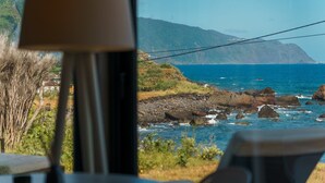 A coastal view with rocky shoreline, a mountain in the background, and a building with a sloped roof. - GuestReady - Relax and Ride the Waves (São Vicente)
