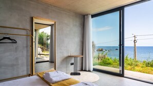 A modern hotel room with a large sliding glass door to the sea, a bed with white linens, a wooden side table, and a mirror. - GuestReady - Relax and Ride the Waves (São Vicente)