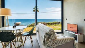 A modern room with a large window overlooking the ocean, a sofa, a table with chairs, and a TV on a stand. - GuestReady - Relax and Ride the Waves (São Vicente)