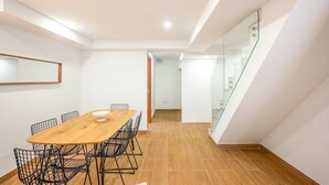 A modern dining area with a wooden table and wire chairs, a glass staircase, and a white interior.