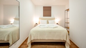 A bedroom with a large mirror, a bed with white linens, two bedside lamps, and a wooden floor.