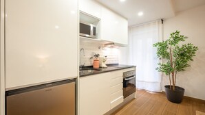 A modern kitchen with white cabinets, a microwave, a sink, and a potted plant.
