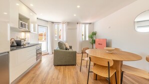 Una cucina moderna con mobili bianchi, un'area pranzo con tavolo e sedie in legno, un divano e una pianta.
