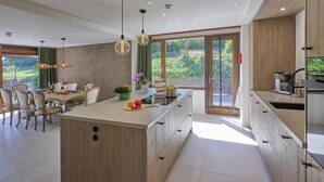A modern kitchen with a central island, wooden cabinetry, and a large window providing a view of greenery. - Luxury house with large garden and wellness (Schinnen)