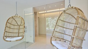 Two hanging wicker chairs with white cushions in a modern room with a glass door leading to a shower area. - Luxury house with large garden and wellness (Schinnen)