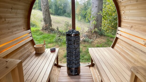A sauna with wooden benches and a stone heater, surrounded by a natural landscape. - Luxury house with large garden and wellness (Schinnen)