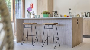 A modern kitchen with a central island, two stools, pendant lights, and a view of the outdoors. - Luxury house with large garden and wellness (Schinnen)