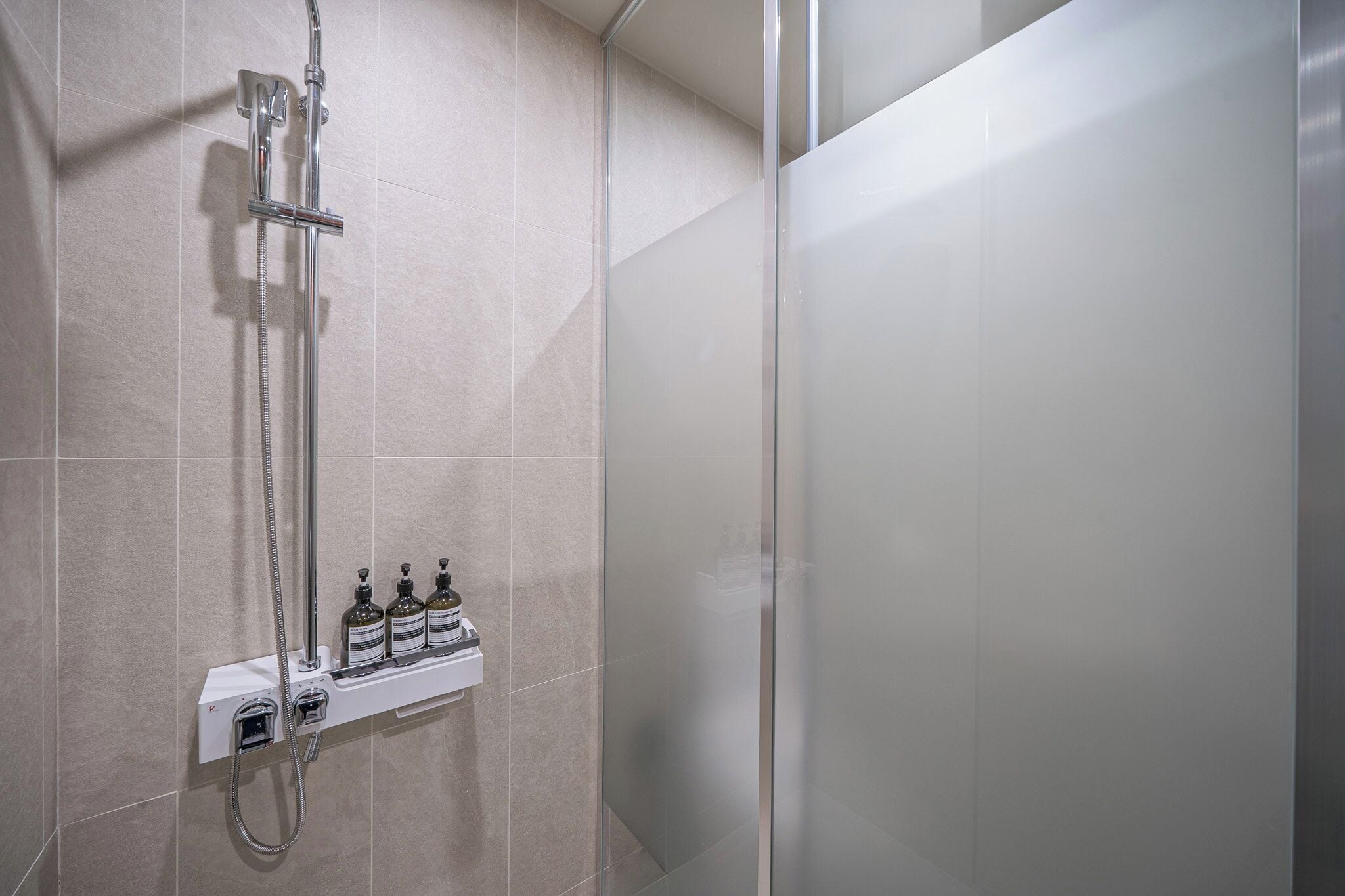 A modern shower with a glass enclosure, a handheld showerhead, and a control panel with multiple bottles.