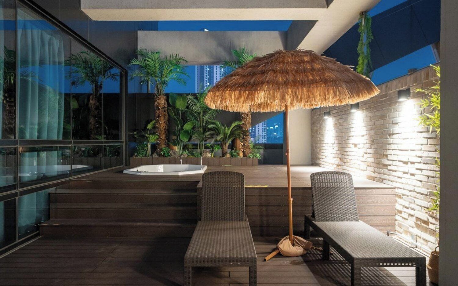 Un área de estar exterior con mobiliario de mimbre, un toldo de paja y un jacuzzi.