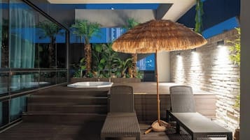Un área de estar exterior con mobiliario de mimbre, un toldo de paja y un jacuzzi.