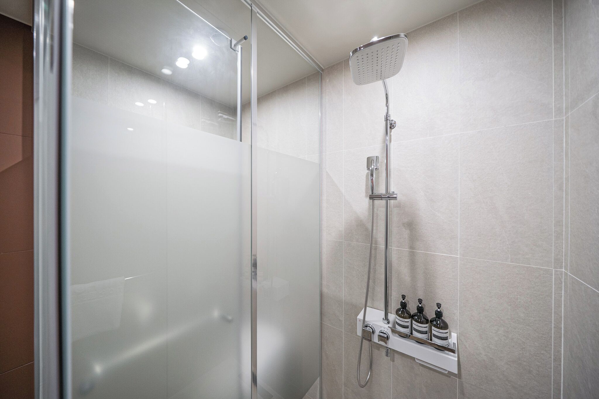 Ducha moderna con puerta de vidrio, cabezal de ducha de mano y dispensador de jabón en la pared.