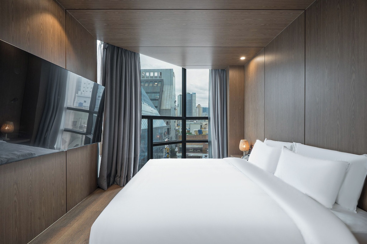 Una habitación de hotel moderna con una cama grande, vistas a la ciudad y un espejo amplio.