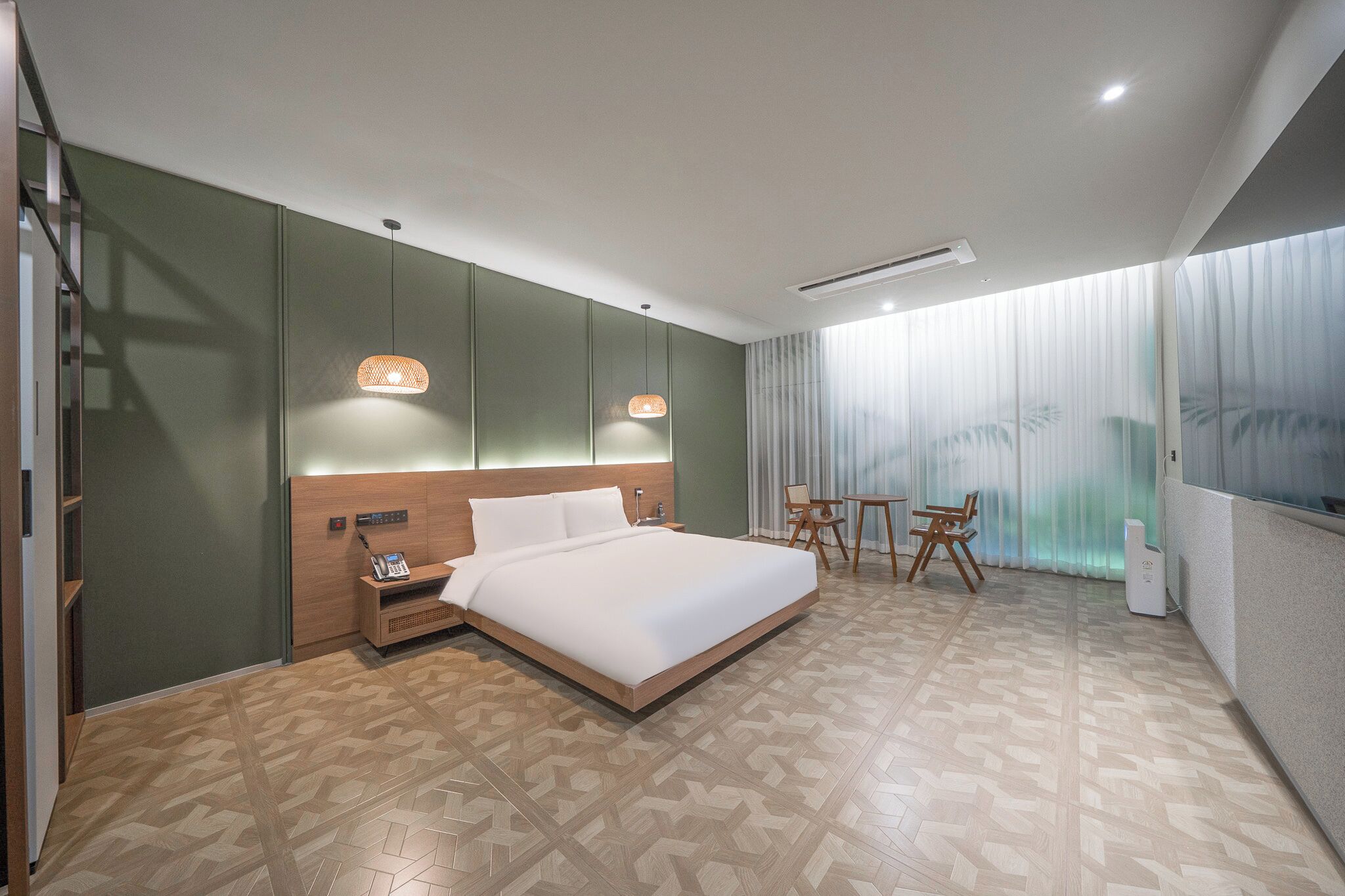 Una habitación de hotel moderna con una cama grande, un escritorio con una silla, una pequeña mesa con sillas y un amplio ventanal con cortinas.